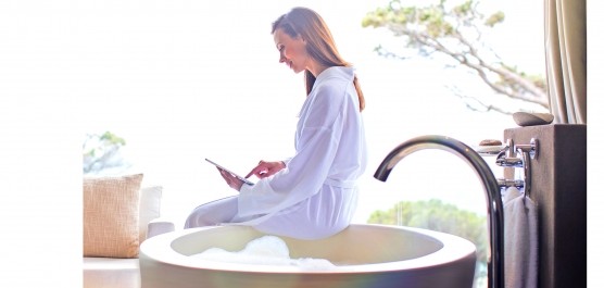 Femme en peignoir assise dans une salle de bain le portable à la main