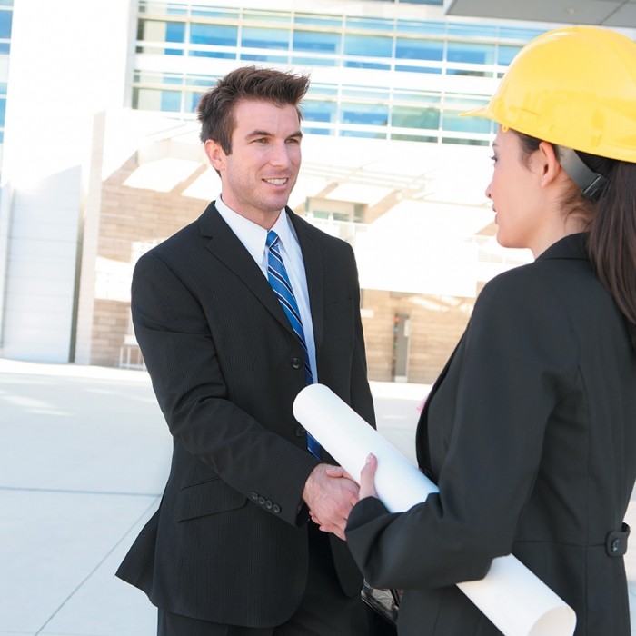 Image d'un homme et d'une femme architecte avec un casque de chantier se serrant la main devant un bâtiment 